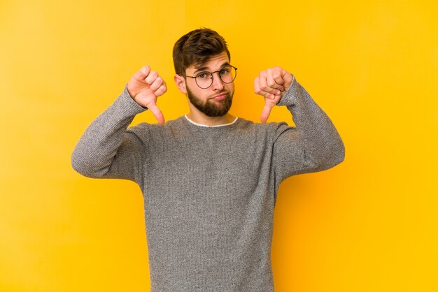 Jeune homme caucasien isolé sur jaune montrant un geste d'aversion, les pouces vers le bas. Concept de Disagreemont.