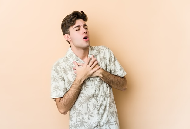 Jeune homme caucasien isolé sur un mur beige a une expression amicale, appuyant sur la paume de la main contre la poitrine. Concept d'amour.