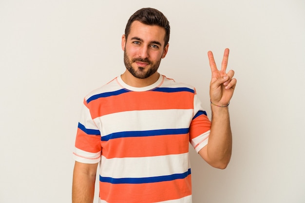 Jeune homme caucasien isolé sur un mur blanc joyeux et insouciant montrant un symbole de paix avec les doigts