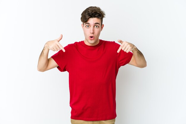 Jeune homme caucasien isolé sur un mur blanc pointe vers le bas avec les doigts, sentiment positif.