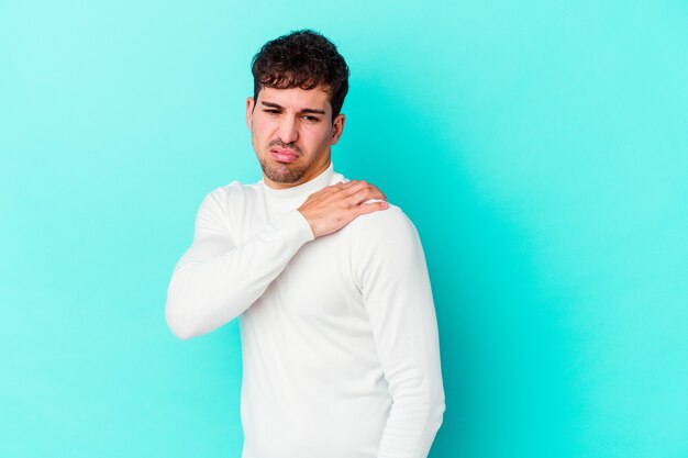 Jeune homme caucasien isolé sur un mur bleu ayant une douleur à l'épaule.