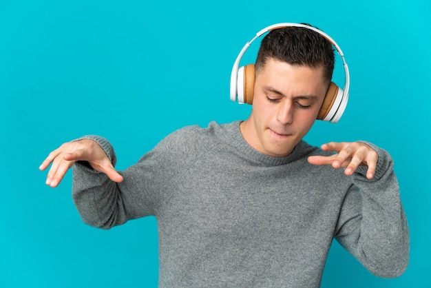 Jeune homme caucasien isolé sur un mur bleu à l'écoute de la musique et de la danse