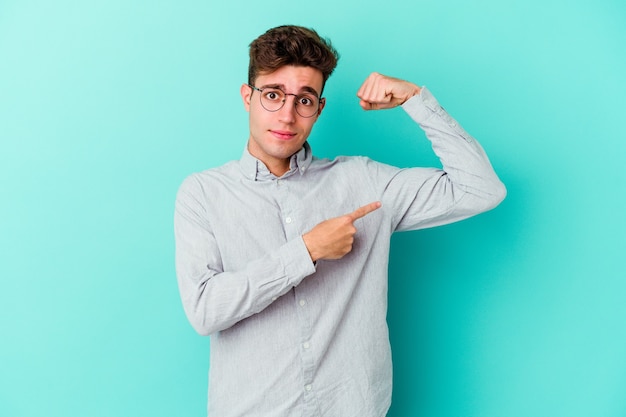 Jeune homme caucasien isolé sur un mur bleu montrant le geste de force avec les bras, symbole du pouvoir féminin