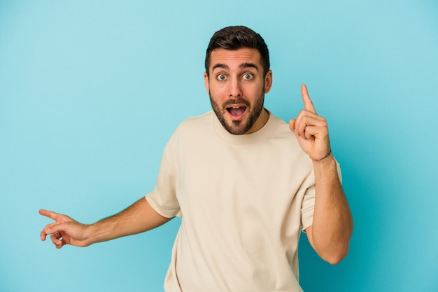 Jeune homme caucasien isolé sur un mur bleu pointant vers différents espaces de copie, en choisissant l'un d'eux, montrant avec le doigt.