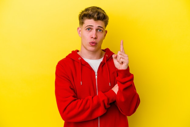 Jeune homme caucasien isolé sur un mur jaune ayant une excellente idée, concept de créativité.