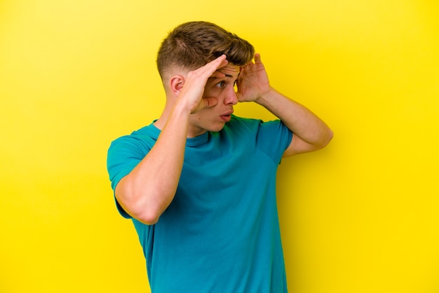 Jeune homme caucasien isolé sur un mur jaune en gardant les yeux ouverts pour trouver une opportunité de succès.