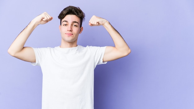 Jeune homme caucasien isolé sur un mur violet montrant le geste de force avec les bras, symbole du pouvoir