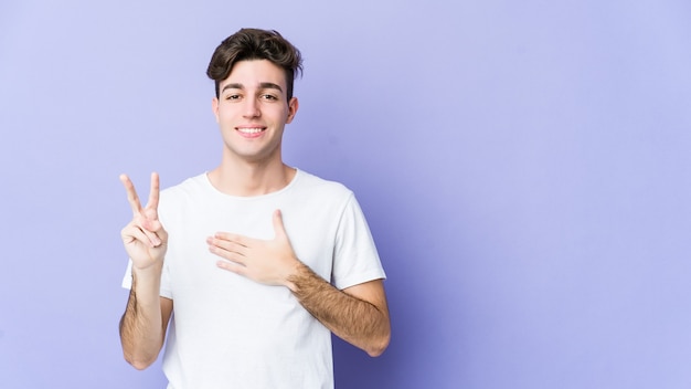 Jeune homme caucasien isolé sur un mur violet prêtant serment, mettant la main sur la poitrine.