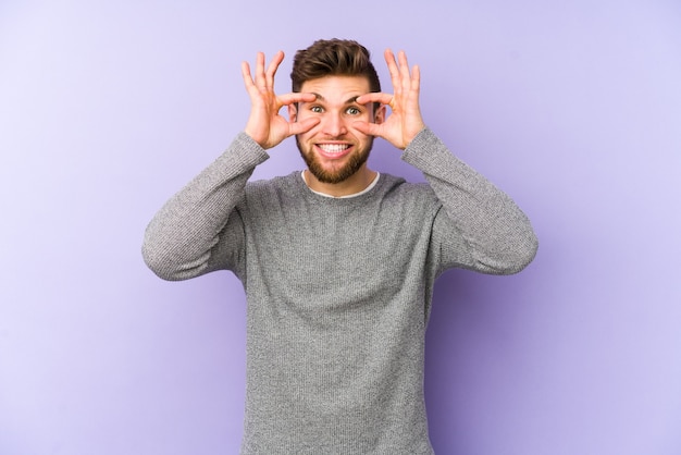 Jeune homme caucasien isolé sur violet gardant les yeux ouverts pour trouver une opportunité de succès.