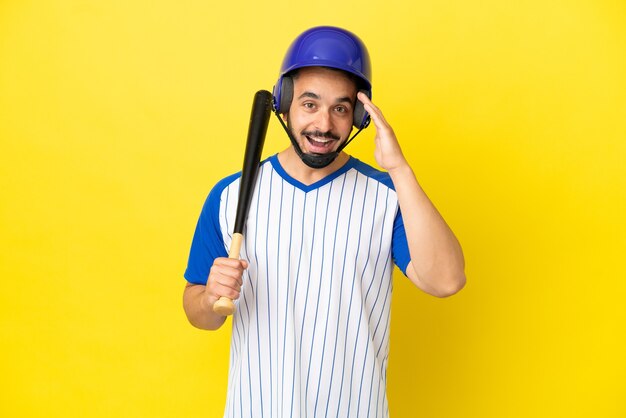 Jeune homme caucasien jouant au baseball isolé sur fond jaune avec une expression faciale surprise et choquée