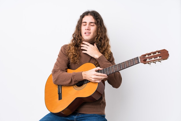 Jeune homme caucasien jouant de la guitare isolé éclate de rire en gardant la main sur la poitrine.