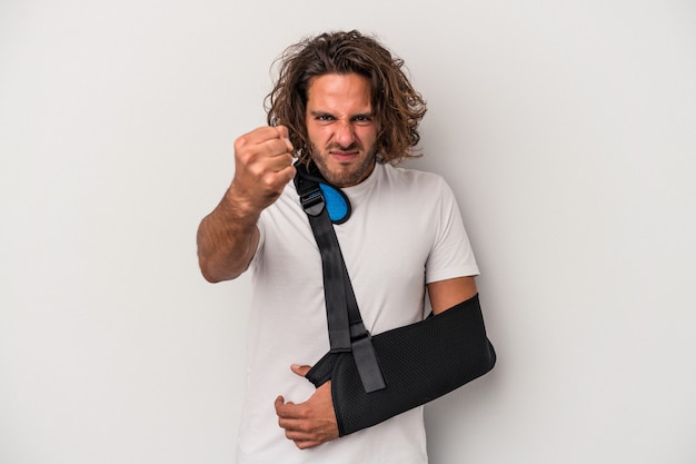 Jeune homme caucasien avec main cassée isolé sur fond gris montrant le poing à la caméra, expression faciale agressive.