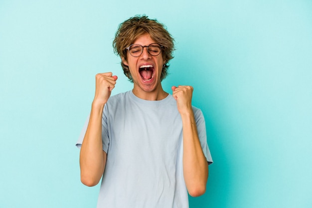 Jeune homme caucasien avec maquillage isolé sur fond bleu acclamant insouciant et excité. Notion de victoire.