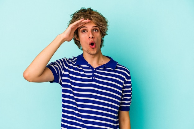 Jeune homme caucasien avec maquillage isolé sur fond bleu crie fort, garde les yeux ouverts et les mains tendues.