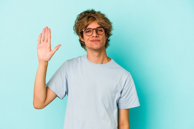 Jeune homme caucasien avec maquillage isolé sur fond bleu souriant joyeux montrant le numéro cinq avec les doigts.