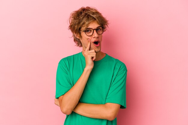 Jeune homme caucasien avec maquillage isolé sur fond rose regardant de côté avec une expression douteuse et sceptique.