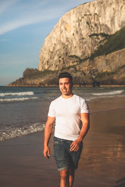 Jeune homme caucasien marchant à la plage