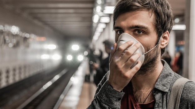 Jeune homme caucasien en masque de protection contre le virus à la station de métro publique en attente de train