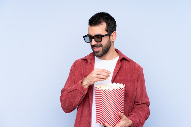 Jeune homme caucasien sur mur bleu avec des lunettes 3d et tenant un grand seau de pop-corn