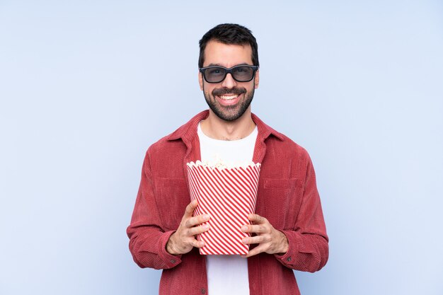 Jeune homme caucasien sur mur bleu avec des lunettes 3d et tenant un grand seau de pop-corn