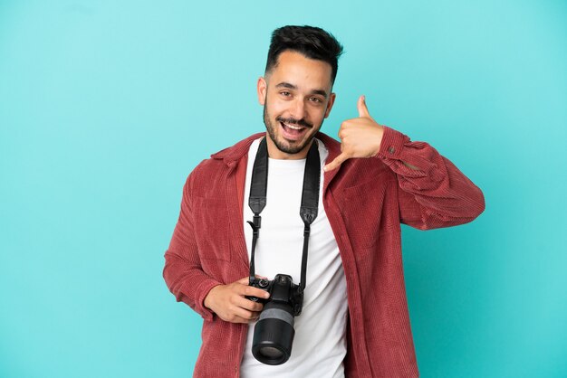 Jeune homme caucasien photographe isolé sur fond bleu faisant un geste de téléphone. Rappelle-moi signe