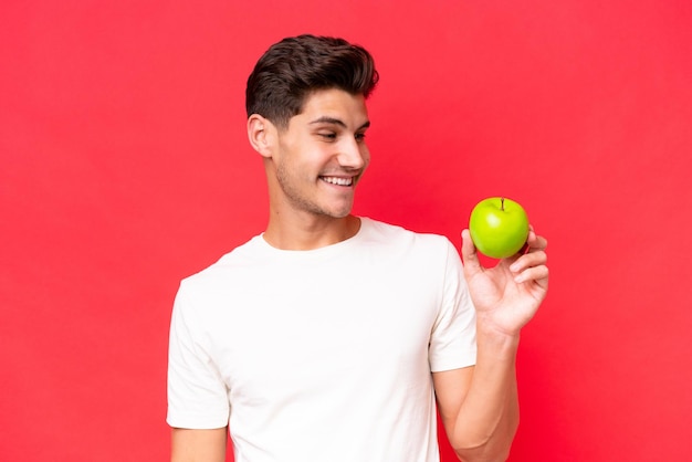 Jeune homme caucasien avec une pomme isolée sur fond rouge avec une expression heureuse