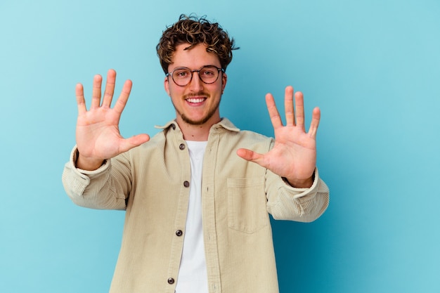 Jeune homme caucasien portant des lunettes isolé sur un mur bleu montrant le numéro dix avec les mains.