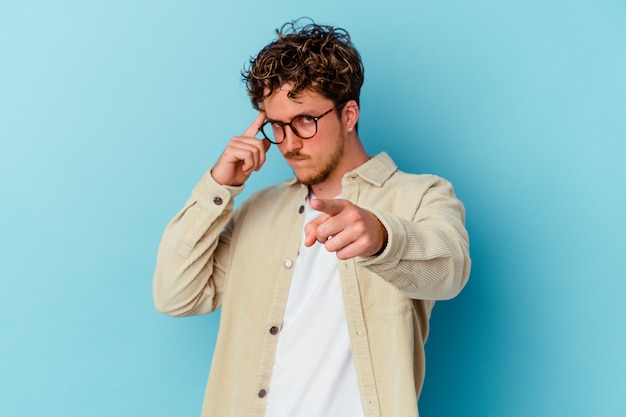 Jeune homme caucasien portant des lunettes isolées sur le mur bleu pointant le temple avec le doigt, pensant, concentré sur une tâche.