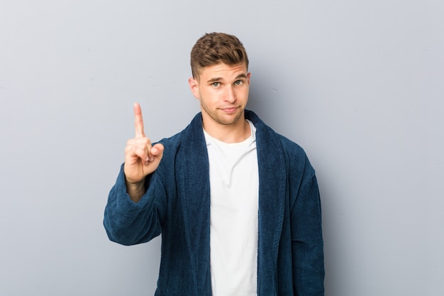 Jeune homme caucasien portant un pyjama montrant le numéro un avec le doigt.