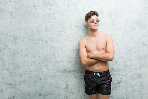 Jeune homme caucasien porte maillot de bain souriant confiant avec les bras croisés.