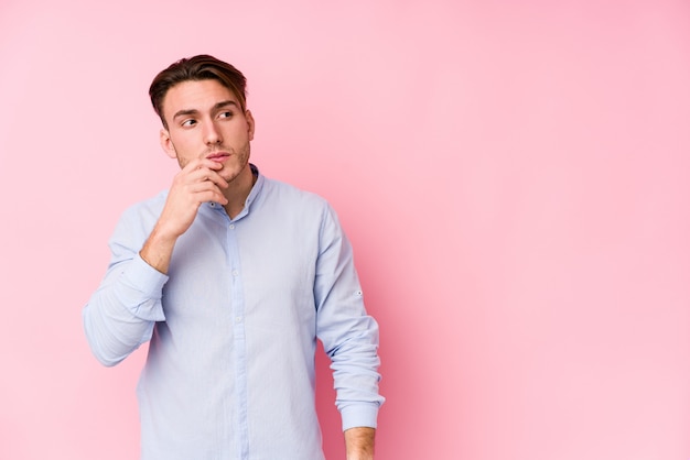 Jeune homme caucasien posant dans un fond rose isolé détendu penser à quelque chose en regardant un espace de copie.