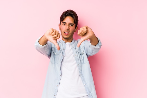 Jeune homme caucasien posant dans un fond rose isolé montrant le pouce vers le bas et exprimant l'aversion.