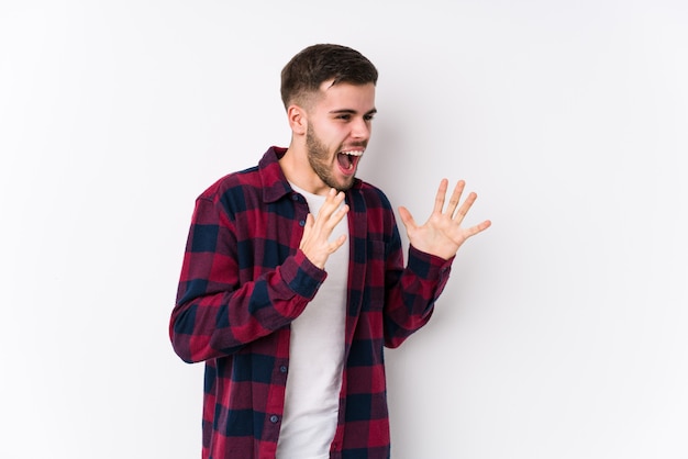 Jeune Homme Caucasien Posant Dans Un Mur Blanc Isolé Crie Fort, Garde Les Yeux Ouverts Et Les Mains Tendues.