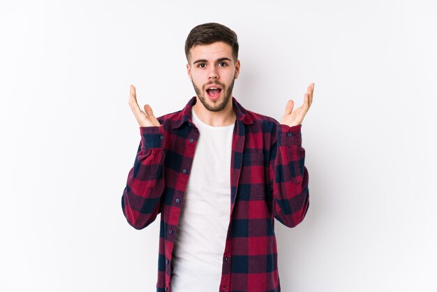 Jeune homme caucasien posant dans un mur blanc surpris et choqué.