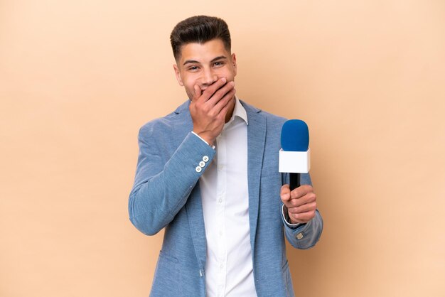 Jeune homme caucasien présentateur de télévision isolé sur fond blanc heureux et souriant couvrant la bouche avec la main