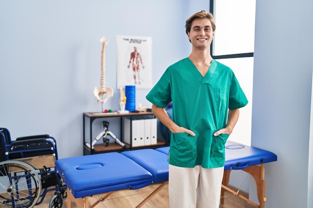 Jeune homme caucasien pysiothérapeute souriant confiant debout à la clinique de réadaptation