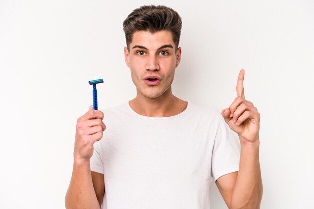 Jeune homme caucasien rasant sa barbe isolé sur fond blanc ayant une bonne idée, concept de créativité.