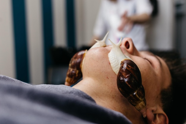 Jeune homme caucasien recevant un massage aux escargots Thérapie et soins de la peau du visage avec des escargots dans un salon de spa Procédure cosmétologique moderne de rajeunissement de la peau