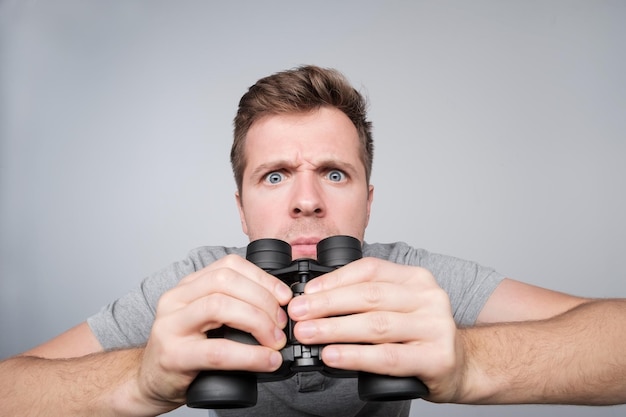 Jeune homme caucasien regardant avec des jumelles devant essayant de voir des détails importants