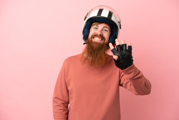 Jeune homme caucasien rougeâtre avec un casque de moto isolé sur fond rose heureux et comptant quatre avec les doigts