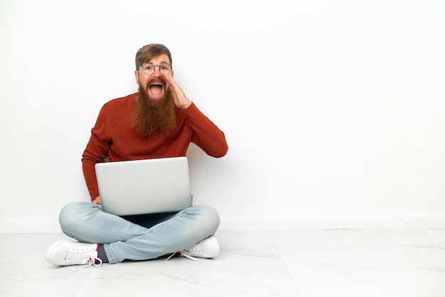 Jeune homme caucasien rougeâtre avec ordinateur portable isolé sur fond blanc criant avec la bouche grande ouverte
