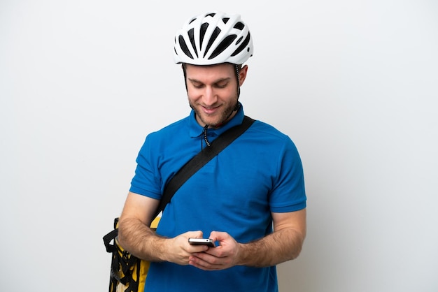 Jeune homme caucasien avec sac à dos thermique isolé sur fond blanc envoyant un message avec le mobile