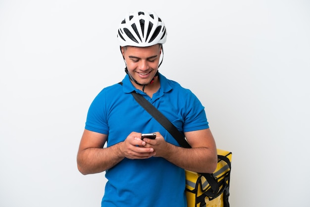 Jeune homme caucasien avec sac à dos thermique isolé sur fond blanc envoyant un message avec le mobile