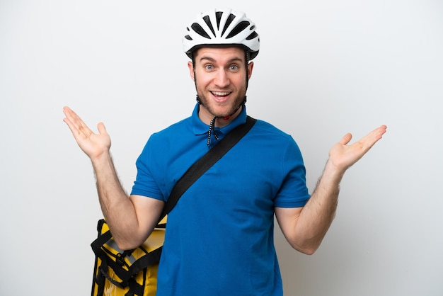 Jeune homme caucasien avec sac à dos thermique isolé sur fond blanc avec une expression faciale choquée