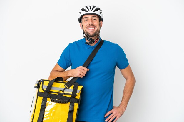 Jeune homme caucasien avec sac à dos thermique isolé sur fond blanc posant avec les bras à la hanche et souriant