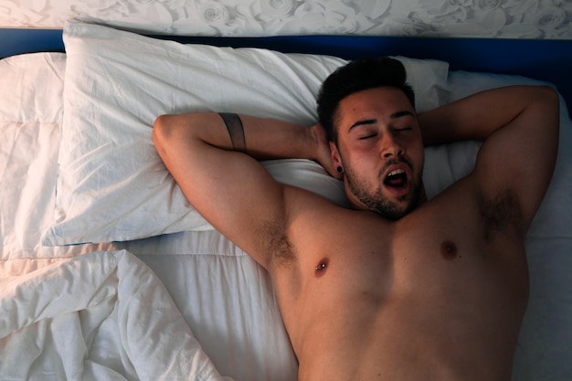 Jeune homme caucasien sexy nu sur le lit sous un angle zénithal