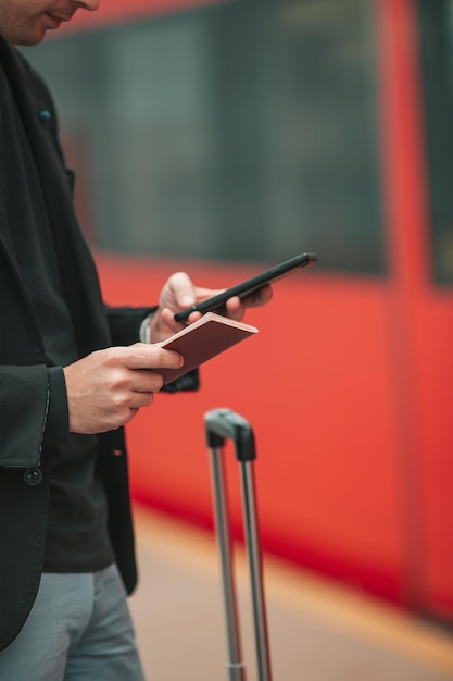 Jeune homme caucasien avec smartphone et bagages à la gare voyageant en train