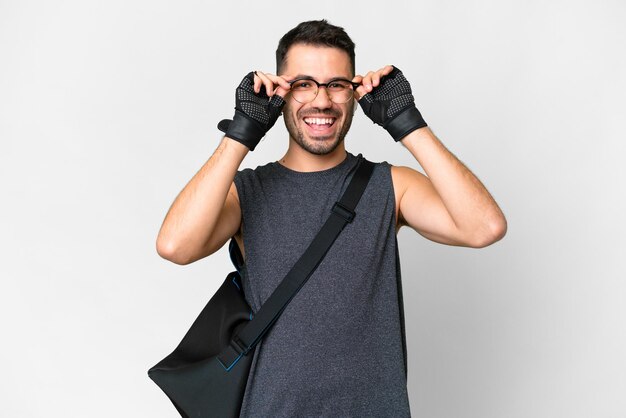 Jeune homme caucasien sport avec sac de sport sur fond blanc isolé avec des lunettes et surpris