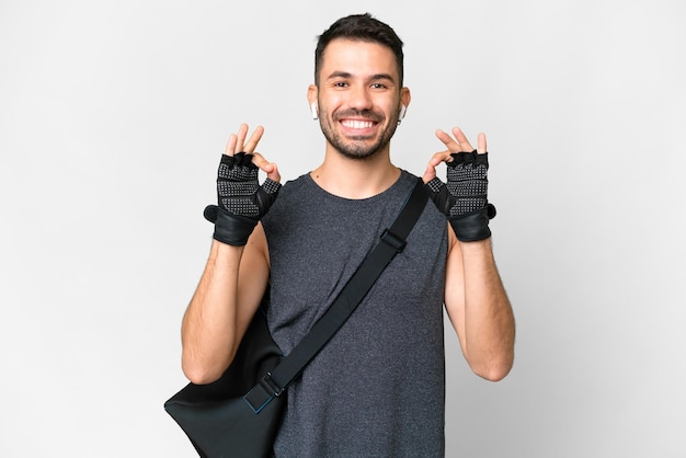 Jeune homme caucasien sport avec sac de sport sur fond blanc isolé montrant un signe ok avec les doigts