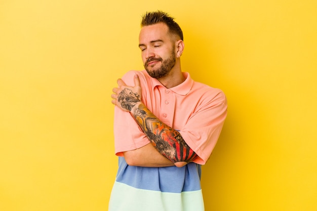 Jeune homme caucasien tatoué isolé sur des étreintes de mur jaune, souriant insouciant et heureux.